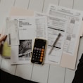 person holding paper near pen and calculator