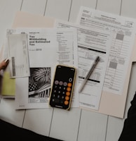 person holding paper near pen and calculator