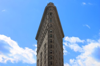 An iconic triangular building with a classic architectural design towers against a bright blue sky with scattered white clouds.