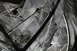 A complex arrangement of metal mesh wires and rods creating an abstract geometric pattern. The mesh creates a layered, intricate design with overlapping grids and shadows, reflecting various shades of gray.