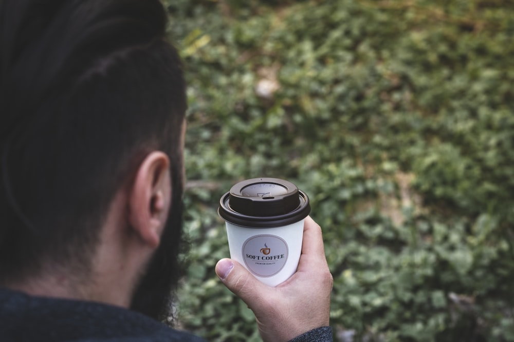 person holding white and black paper cup with lid