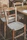 Two rustic wooden chairs with woven seats are placed next to a wooden table. The chairs and table have a worn, vintage look, suggesting an antique or retro setting. The texture of the woven seats contrasts with the weathered wood of the chairs.