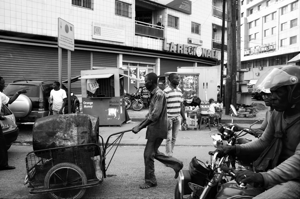 Photographie en niveaux de gris d’un homme poussant une remorque avec un tambour