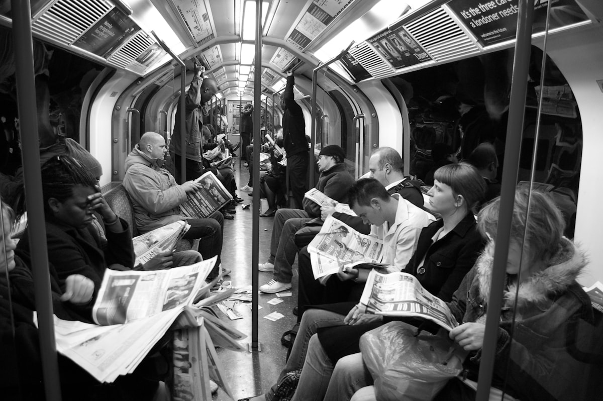 People sitting in a subway carriage reading newspapers.