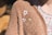 A close-up of a textured brown sweater adorned with embroidered flowers, one white with a yellow center and one small green leaf design. Part of the person's floral-patterned shirt is visible underneath the sweater.