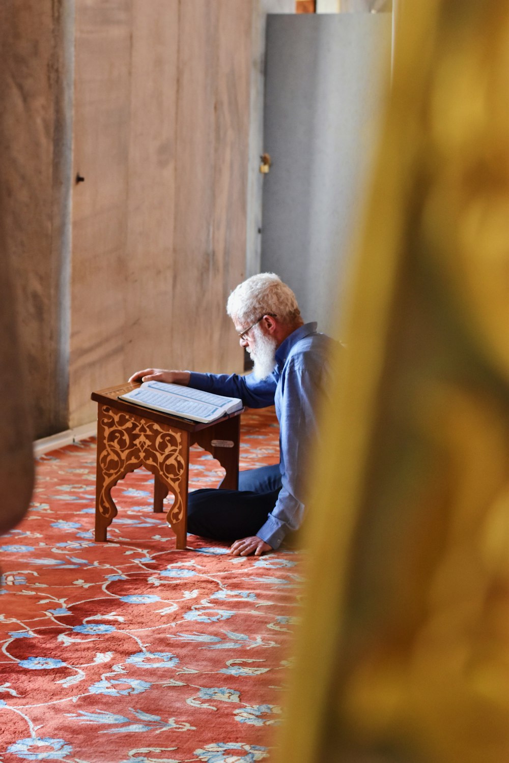 man sitting on area rug reading book on book stand