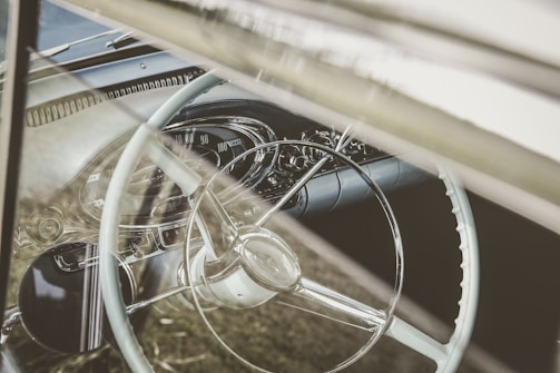 The dashboard view inside a vintage car, with a glimpse of the steering wheel and speedometer.