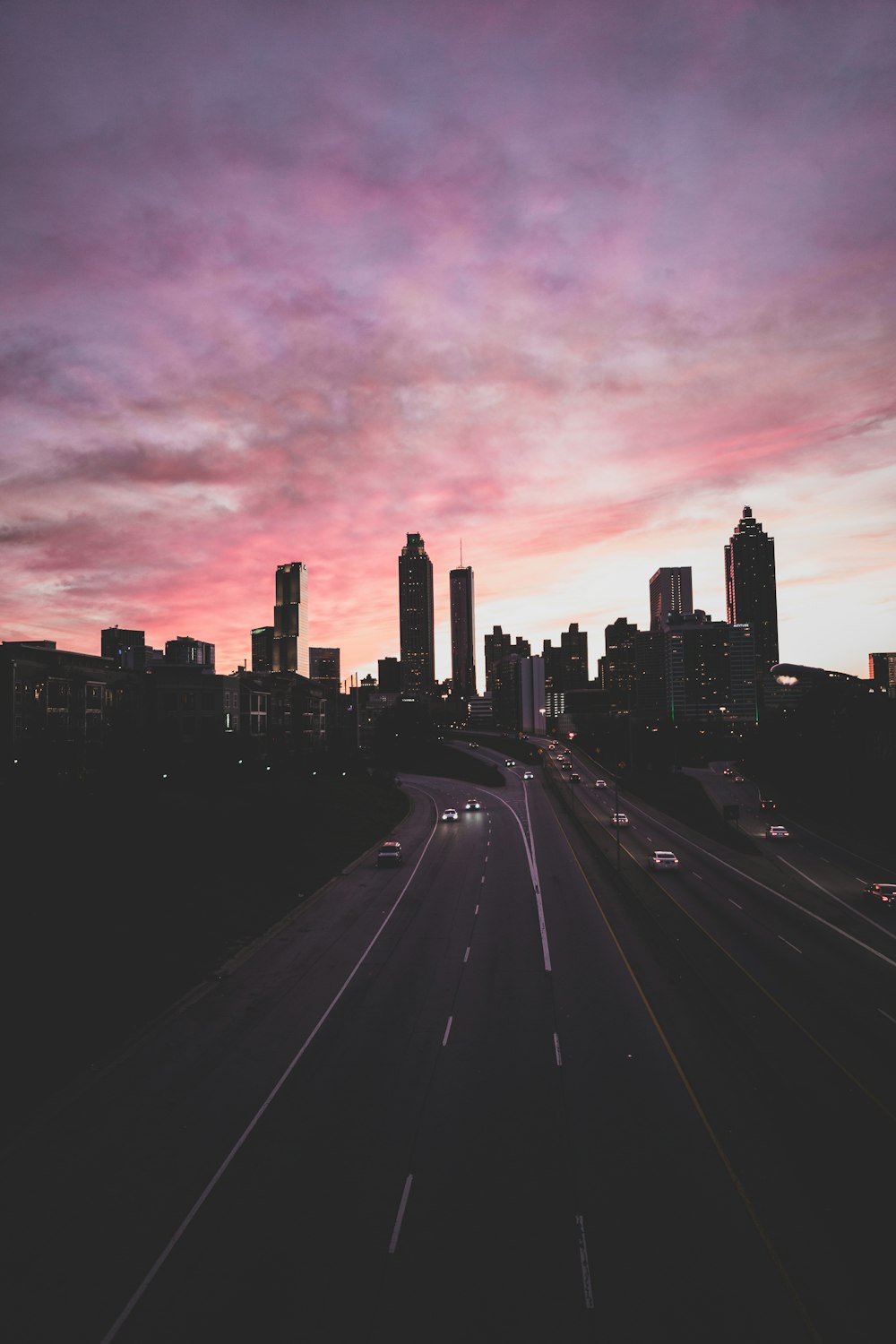 日没時の灰色とピンク色の曇り空の下、高速道路を走行する車