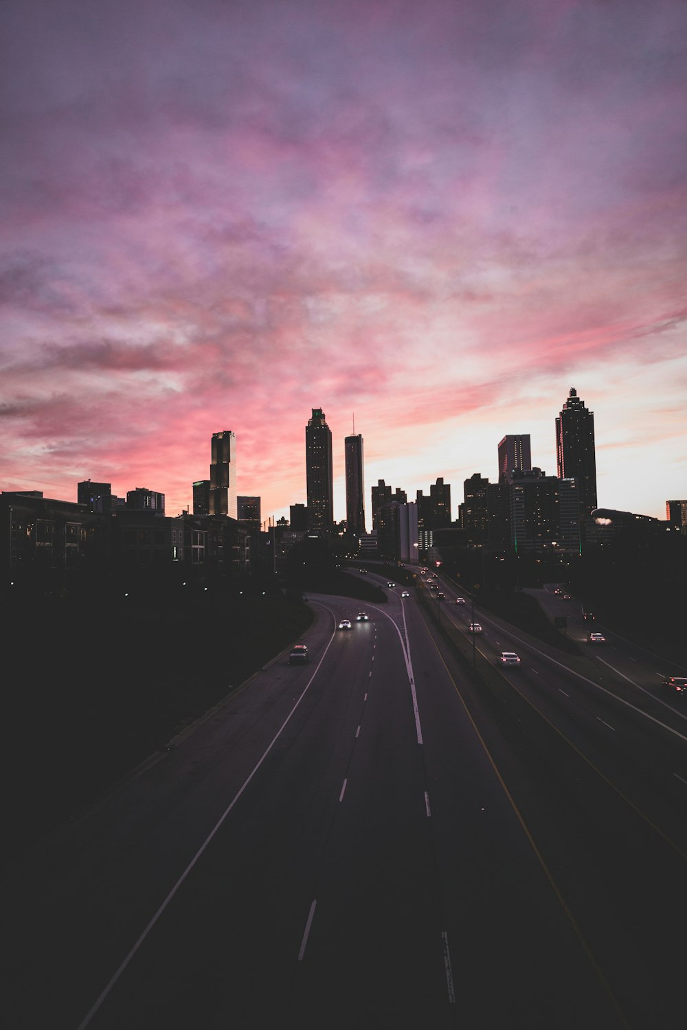 cars traveling on expressway under grey and pink cloudy sky during sunset