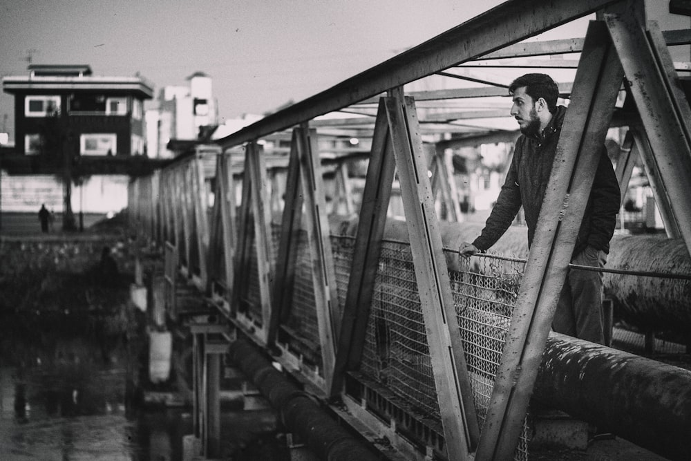 grayscale photo of man standing on bridge