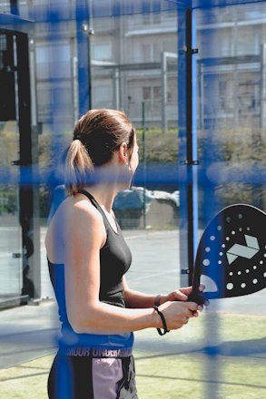 A professional padel coach giving a lesson to a small group of attentive players on a sunny outdoor court in Spain.