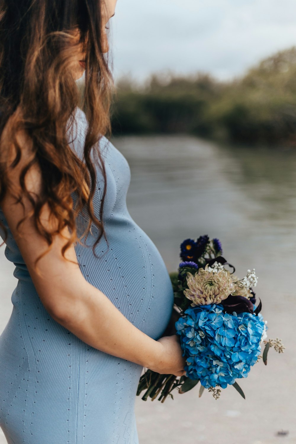 pregnant woman in blue sleeveless dress holding bouquet of flowers