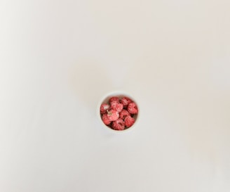 A spoonful of vibrant raspberry powder spilling gently onto a white ceramic plate.