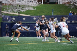 A dynamic action shot of women playing lacrosse on the field.