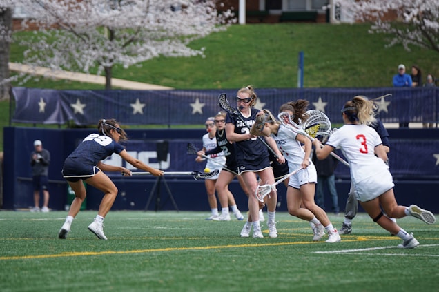 A dynamic action shot of women playing lacrosse on the field.