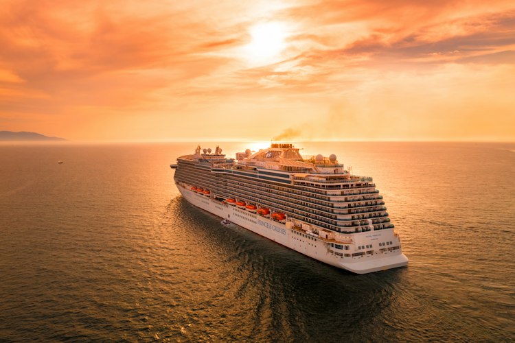 Large cruise ship docked at a port with passengers walking along the pier