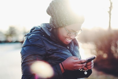 smiling woman wearing black coat using smartphone phone google meet background