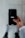 A person holds a smartphone displaying the Uber logo on the screen. The phone is oriented vertically and appears to be in use. The person is dressed in a light-colored sleeve, and the background is a neutral, blurry surface.