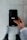 A person holds a smartphone displaying the Uber logo on the screen. The phone is oriented vertically and appears to be in use. The person is dressed in a light-colored sleeve, and the background is a neutral, blurry surface.
