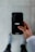 A person holds a smartphone displaying the Uber logo on the screen. The phone is oriented vertically and appears to be in use. The person is dressed in a light-colored sleeve, and the background is a neutral, blurry surface.