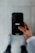 A person holds a smartphone displaying the Uber logo on the screen. The phone is oriented vertically and appears to be in use. The person is dressed in a light-colored sleeve, and the background is a neutral, blurry surface.