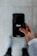 A person holds a smartphone displaying the Uber logo on the screen. The phone is oriented vertically and appears to be in use. The person is dressed in a light-colored sleeve, and the background is a neutral, blurry surface.