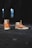 A pair of cream-colored high-top sneakers with bright orange accents and orange laces stands on a rough, dark surface. The sneakers display text on the side and have a distinctive design. The background is dimly lit, creating a contrast with the footwear.