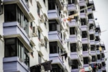 A series of residential apartment balconies, each with windows and air conditioning units. Clothes hang from lines stretched across the balconies, drying in the open air.