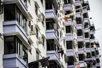 A series of residential apartment balconies, each with windows and air conditioning units. Clothes hang from lines stretched across the balconies, drying in the open air.