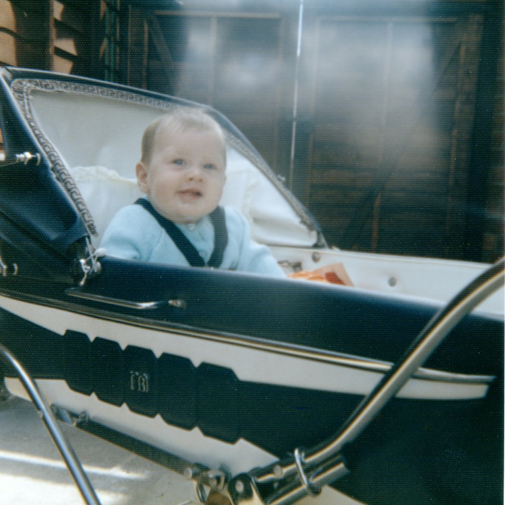 baby sitting on black stroller smiling