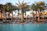 A smiling guest relaxing on a sun lounger by the hotel pool with palm trees in the background.