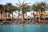 A smiling guest relaxing on a sun lounger by the hotel pool with palm trees in the background.