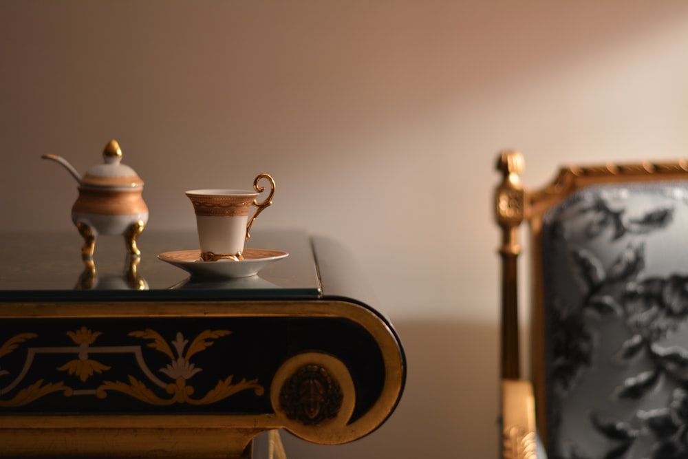 white and gold ceramic cup and saucer near teapot on brown wooden table