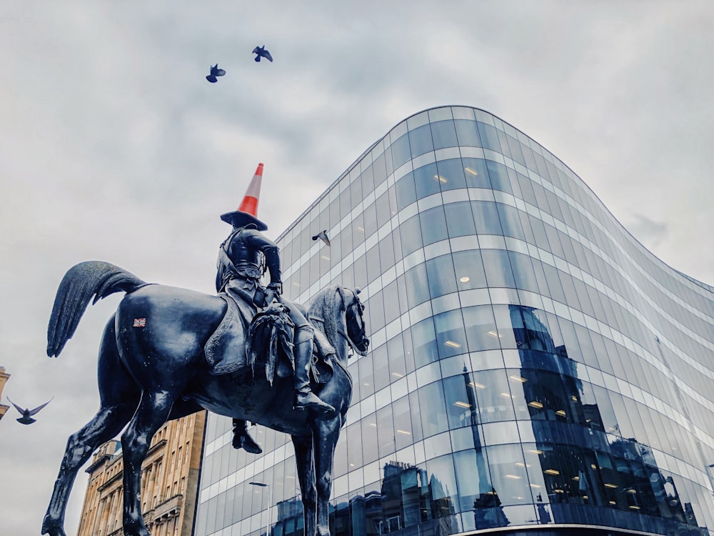 man riding on horse statue near glass high-ride building