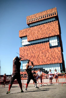 A dynamic moment from a stage combat class where two students practice a choreographed sword fight under instructor supervision.