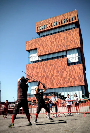 A dynamic moment from a stage combat class where two students practice a choreographed sword fight under instructor supervision.