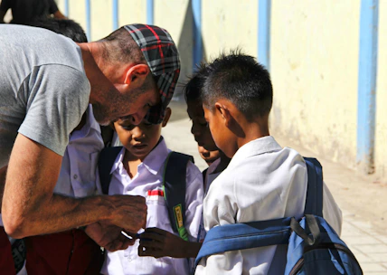 Volunteers distributing school supplies to eager students in a sunny outdoor setting.