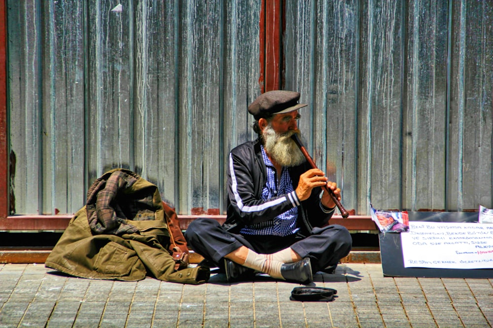 man playing flute sitting on the side of the street