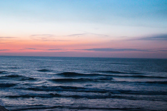 A serene horizon over a calm ocean at dusk, with soft beige and charcoal tones blending into the sky.