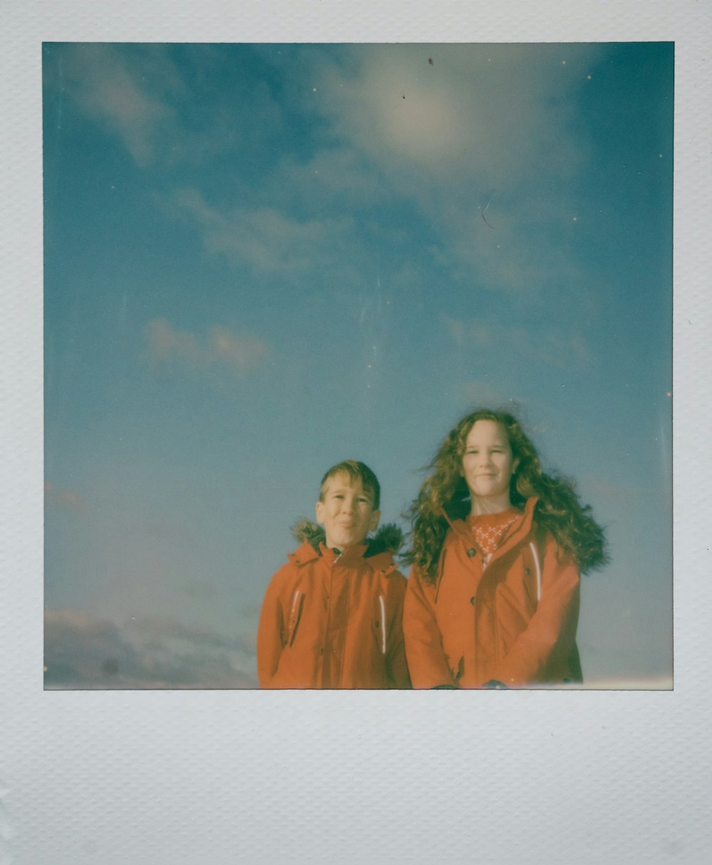 girl and boy wearing orange jackets standing