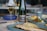 A wine bottle and a filled glass are positioned on a dining table. The table features a selection of dishes, including a plate with a grilled fish in the foreground and side dishes in blue bowls. The setting suggests an elegant meal.