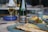 A wine bottle and a filled glass are positioned on a dining table. The table features a selection of dishes, including a plate with a grilled fish in the foreground and side dishes in blue bowls. The setting suggests an elegant meal.