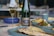 A wine bottle and a filled glass are positioned on a dining table. The table features a selection of dishes, including a plate with a grilled fish in the foreground and side dishes in blue bowls. The setting suggests an elegant meal.