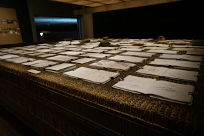 A rustic wooden table displaying several sketchbooks stacked with worn leather covers.