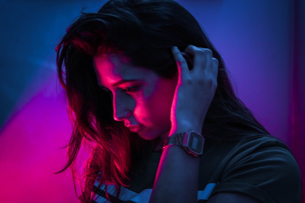 woman in gray shirt standing near pink light holding her hair