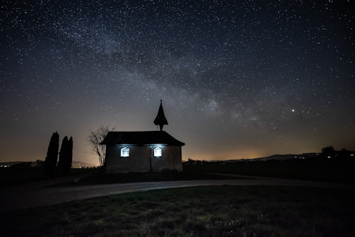 A serene night sky with golden stars shining over a calm, blue European-style chapel.