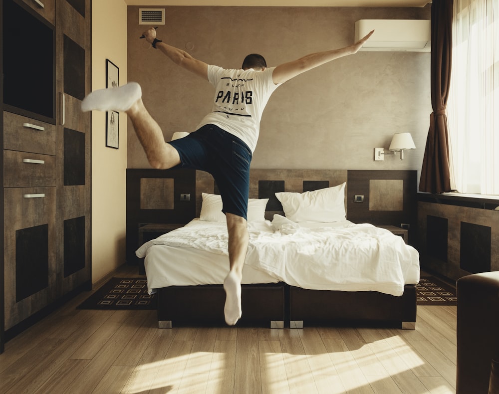 man wearing white shirt about to jump on bed