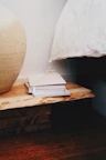 Close-up of artisanal ceramic vase on a wooden bedside table with soft linen bedding.