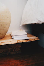 Close-up of artisanal ceramic vase on a wooden bedside table with soft linen bedding.