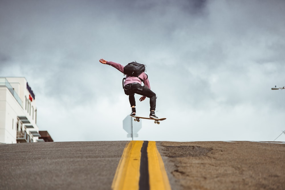 man wearing pink shirt with backpack doing skateboard trick